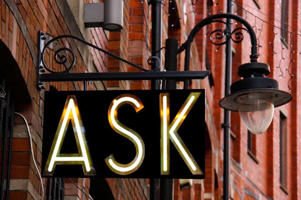A lit sign displaying the word ‘ASK’ mounted on the exterior of a brick building