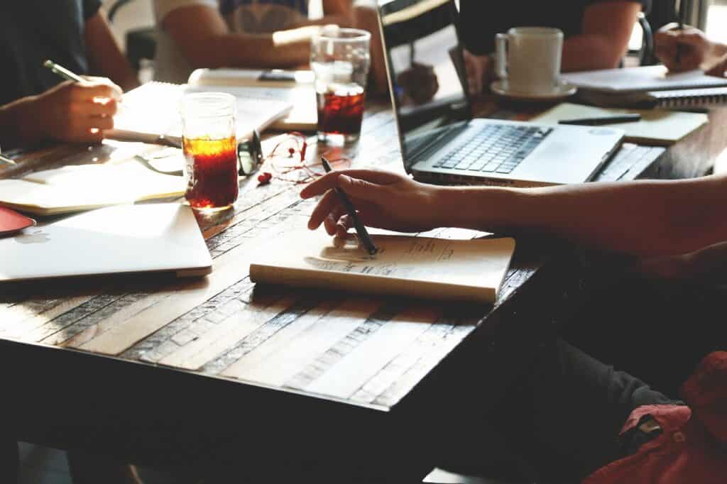 People seated around a table taking notes and working on laptops during a collaborative meeting.