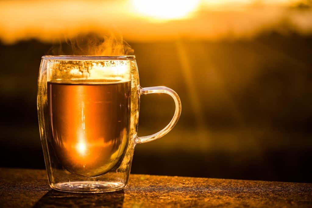 A glass mug of hot tea placed outdoors in warm sunlight, with steam rising from the cup
